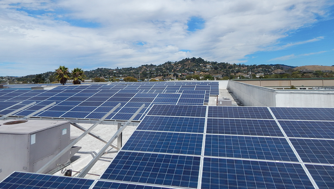 rooftop solar system on commercial building, tree filled hillsides, clear sky, clouds