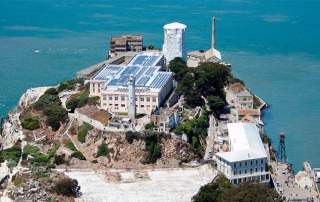 aerial view of Alcatraz island, abandoned prison building, watch tower, trees, calm ocean water
