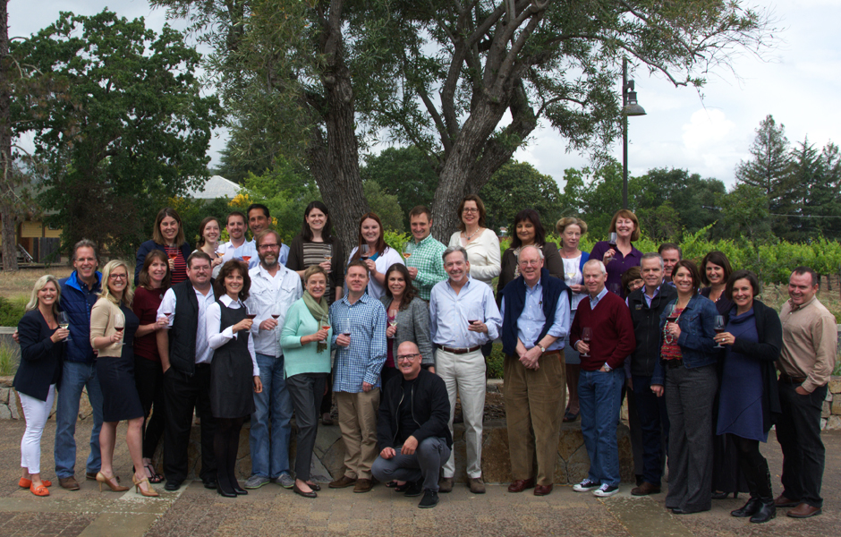 over thirty members standing, posing for camera, smiling, holding wine glass, large oak tree in background, clear sky
