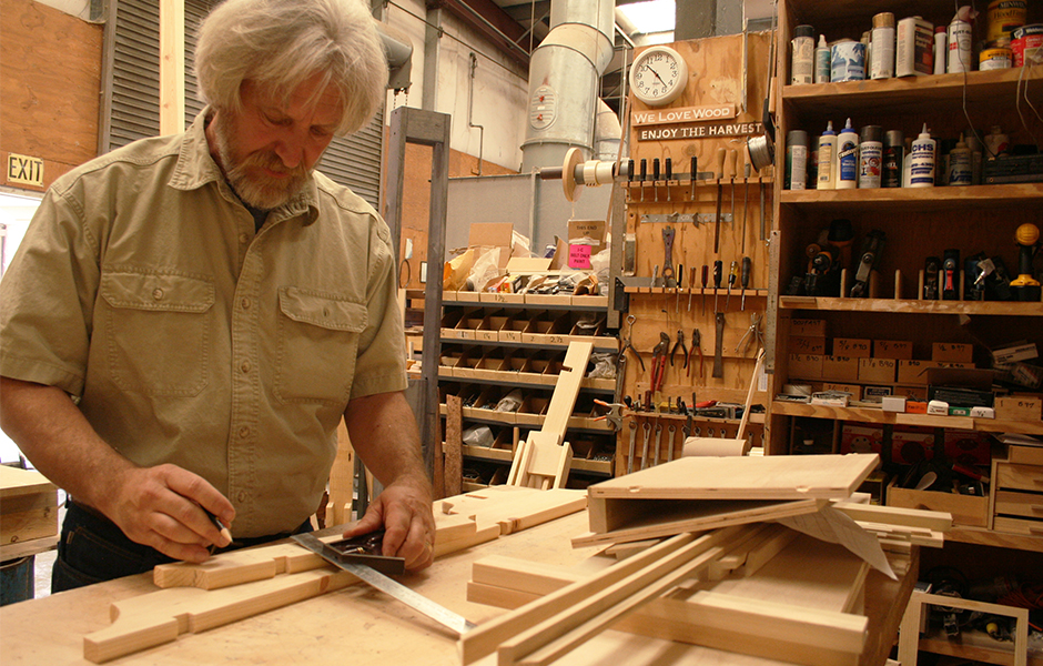 Jack Ruszel, looking down at custom cut wood, measuring tool, pencil for marking in hand, inside professional wood shop