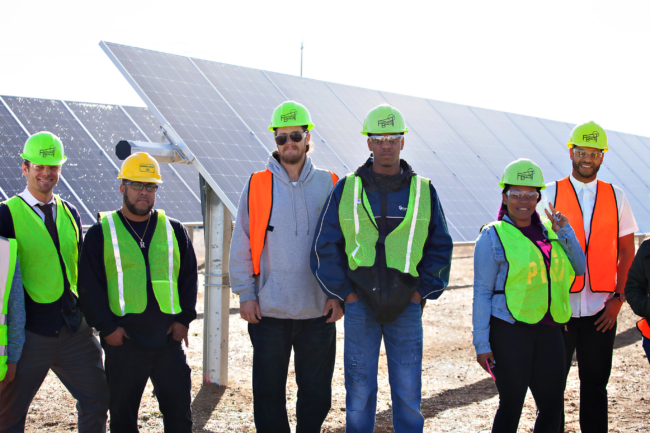 MCE staff member and five local call center trainees stand in front of ground mounted solar arrays at MCE Solar One
