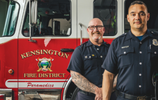two Kensington firefighters stand straight, in front of fire truck, decal says Kensington Fire District paramedics