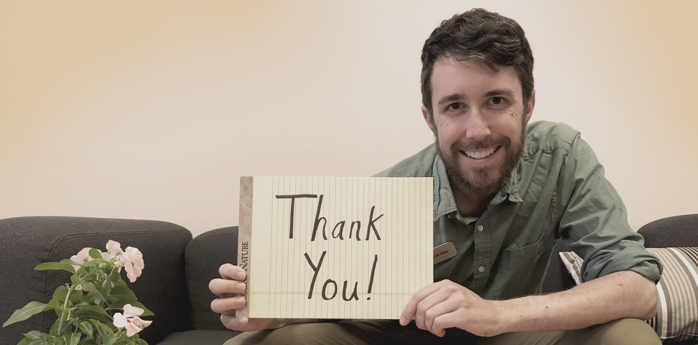 smiling MCE staff member Brett Wiley sitting on couch, holding note pad, says thank you