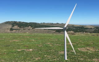 commercial grade wind turbine in grass field, hills in distance, clear sky