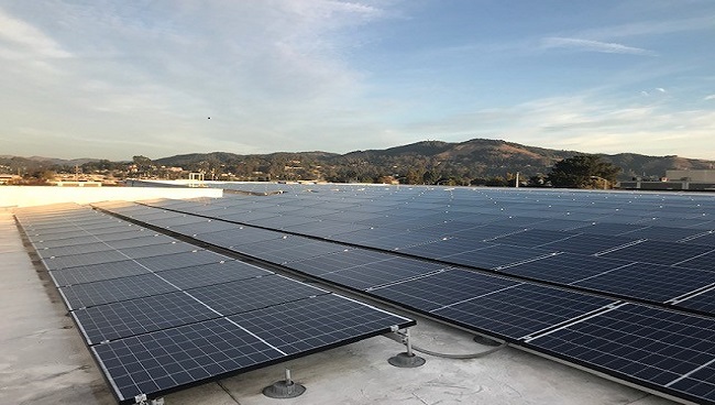 large scale rooftop solar system on commercial building, tree filled hillsides, clear sky, dusk