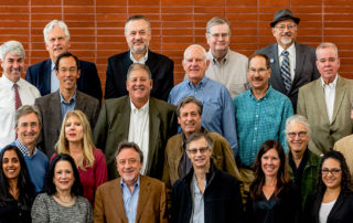 twenty one MCE board members, and leadership smile for camera, brick wall in background