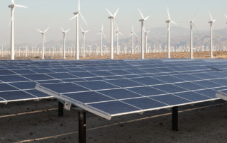 desert land, ground mounted solar panels, one hundred plus wind turbines in distance, mountains, overcast sky