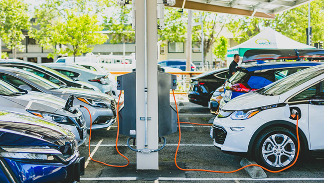 Neun Elektrofahrzeuge geparkt, an Ladeanschlüsse angeschlossen MCE Büroparkplatz San Rafael unter Carport-Schattenstruktur