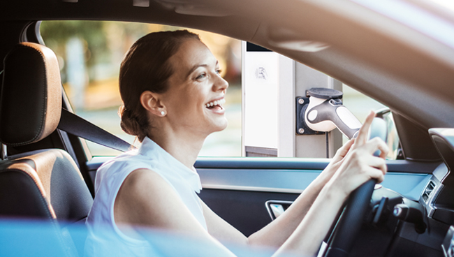 young woman smiling while driving electric vehicle, sitting in driver seat, both hands on wheel and looking ahead