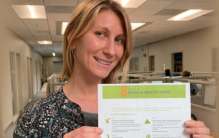 MCE Customer Programs Manager, Michelle Nochisaki, holds up flyer in office, says eight elements of a Green and Healthy Home