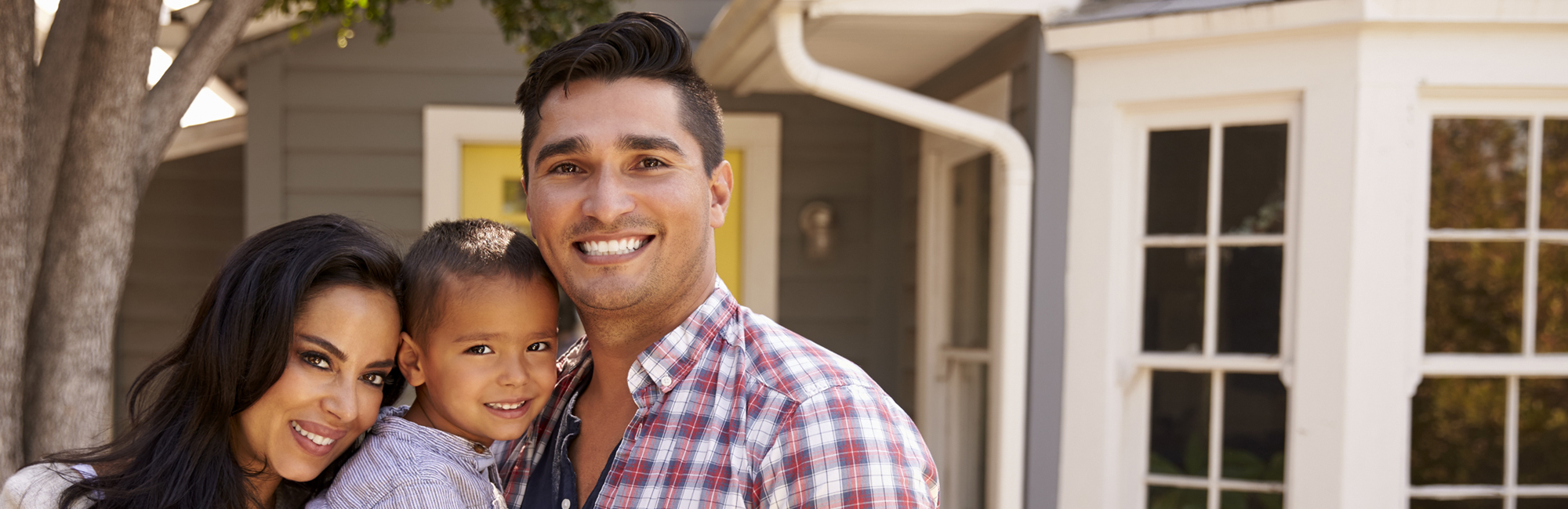 wife, son and father, smiling and hugging, in front of their single family home