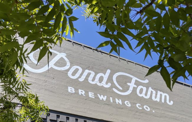 front entrance outisde of brewery, close up view, building says Pond Farm Brewing Company, tree branches in view, clear sky