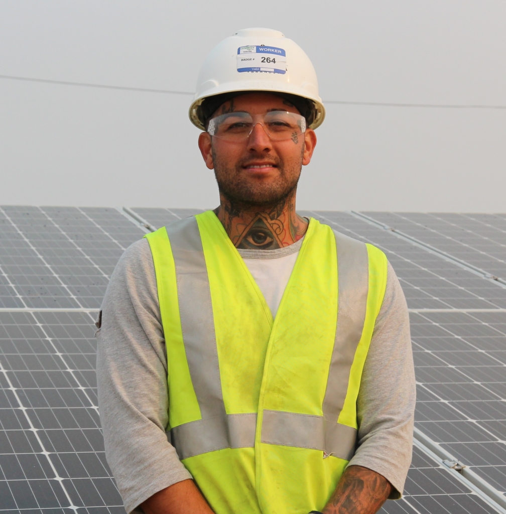 MCE Solar One construction worker, wearing safety vest and glasses, hard hat, smiling in front of solar array