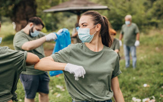 Two young women wearing masks greet eachother at a local environmental clean up event